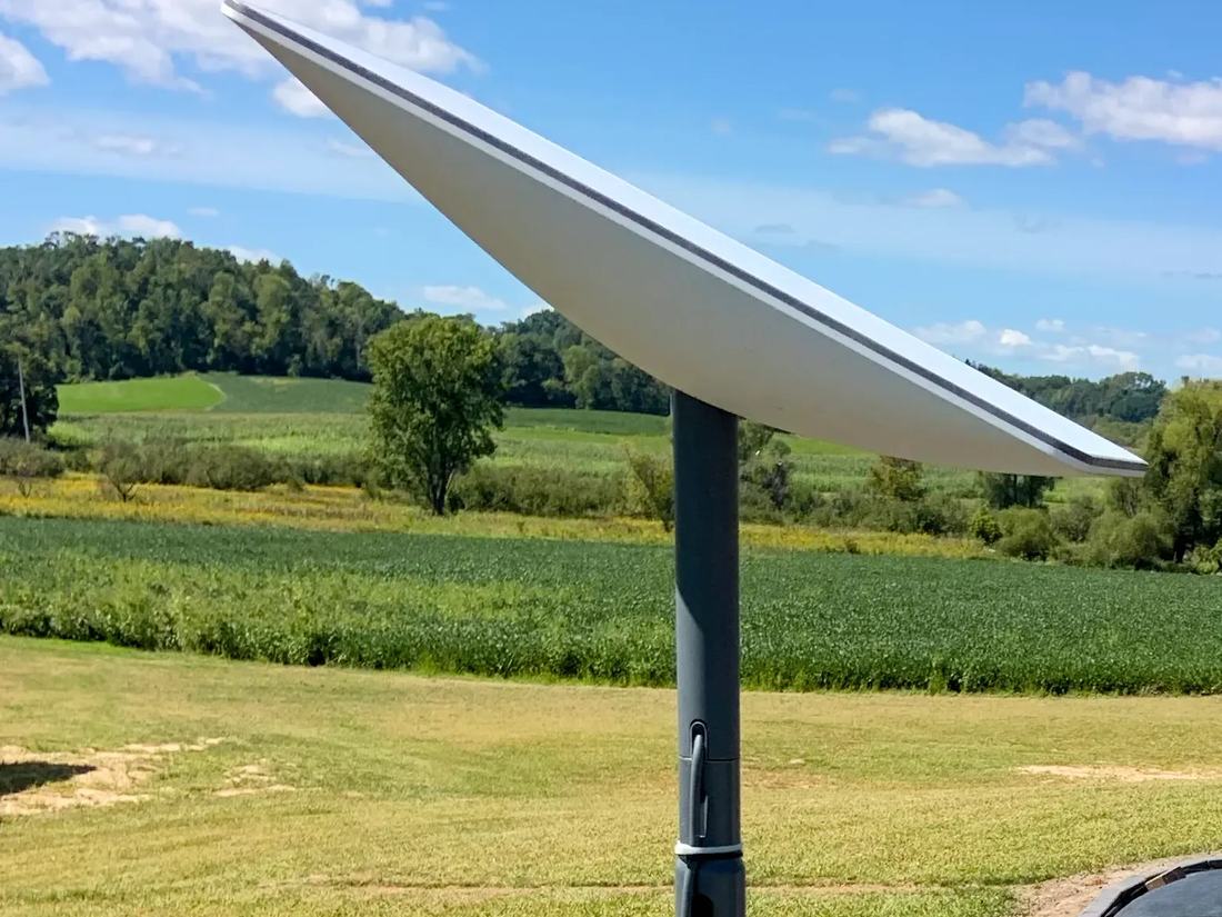A Starlink dish on a pole mount in front of open green farmland under a blue sky